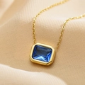 Makroaufnahme einer goldenen Edelstahlkette mit blauem Zirkon-Anhänger auf Seidenstoff - Blau