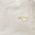 Detailansicht eines minimalistischen goldenen Wellenrings auf künstlerischem weißem Papier - US 6 / Dünne V-Form