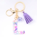 Close-up of resin letter L keychain with purple tassel and colorful stones - Letter L
