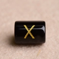 Macro shot of a black cylindrical bead with a gold-stamped letter X for DIY jewelry - Letter X