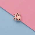Makroaufnahme von roségoldenem China-Anhänger Fu auf rosa und blauem Papier - Roségold