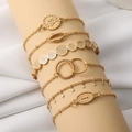 Detail van 6-delige gouden armbandset met schelp- en bladhangers op een beige standaard - Schelp 6-delige Set / Goud