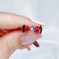 Dettaglio macro di un anello argentato con fiocco a farfalla rosso e pietra centrale brillante - Stile fiocco rosso rubino