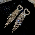 Dettaglio di orecchini a cuore con lunghe nappe di strass brillanti su sfondo nero - Oro / Oro