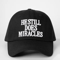 Dettaglio del ricamo 3D bianco He Still Does Miracles su un cappellino in cotone nero - Nero
