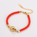 Macro shot of red braided lucky bracelet with interlocking Roman numeral rings - Gold