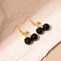 Detail view of black resin cherry earrings with gold metal leaf on stone background - Black Cherry Ear Hook