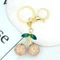 Detail of a gold cherry keychain with sparkling champagne rhinestones and green crystal leaves - Champagne Rhinestone Cherry