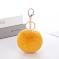 Close-up of bright yellow faux rabbit fur keychain with golden lobster clasp on white surface - Turmeric