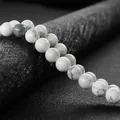 Polished natural white turquoise 8mm round beads on a textured black display cylinder - White Howlite
