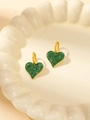Elegante goldene Herzohrringe mit grünen Kristallen auf einem Keramikteller - Herz-Ohrringe voll mit grünem Zirkon