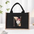 Black canvas tote bag featuring a gold letter N with floral accents and jute trim - Bronze Floral Letter N