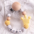 Detail of beech wood pacifier clip with silicone beads and crown pendant forming BABY - Yellow
