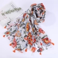Flat lay of a floral cotton scarf with orange tassels beside a magazine and greenery - Style 4