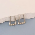 Detail of silver trapezoid earrings with heart elements on a white stone background - Silver Beaded Heart