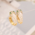 Macro detail of gold snake earrings with white enamel and sparkling green cubic zirconia - White