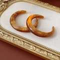Dettaglio degli orecchini a C in resina ambrata con motivo tartarugato su tessuto bianco - Perno per orecchini in argento - Caffè