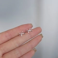 Detailed macro view of small silver bow stud earrings held on a finger for scale - Tassel Bowknot / Silver