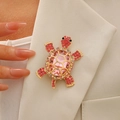 Broche de tortuga con pedrería rosa en la solapa de una chaqueta beige de moda - Rosa