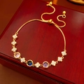 Golden bracelet with pink, blue, purple stones and clover charms on a wood surface - Gold