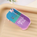 Detail van de glitterende PVC haarklem in pilvorm met Chill Pill tekst en een smiley - Paars en Groen Gradiënt