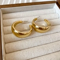 Makro-Detail von klobigen goldenen C-Ohrringen mit poliertem Hochglanz-Finish auf Leinen - Gold (mit Silbernadel)