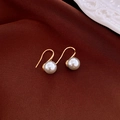 Detalle de pendientes minimalistas de oro con perlas grises sobre fondo de tela sedosa - Gancho de Perla Gris 8mm