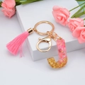 Pink resin letter J keychain with tassel and gold flakes on white stand - Letter J