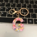 Detail of letter G resin keychain with colorful heart sequins on a laptop keyboard - Letter G