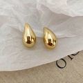 Nahaufnahme goldener Tropfenohrringe mit glattem Finish auf strukturiertem weißem Papier - Gold Wassertropfen