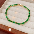 Detail eines vergoldeten Armbands mit smaragdgrünen Zirkonia auf beigem Kissen - Armband - Gold - Grün