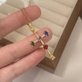 Collana dorata con ciondolo a croce rosa e gemme colorate tenuta su una scatola di legno - Croce Colorata