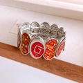 Dettaglio macro di un bracciale vintage in smalto rosso e arancione con motivi stella e G - Argento-Giallo-Rosso
