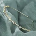 Minimalist gold leaf headband with rhinestones and white pearls on green fabric background - Square Rhinestone Luxury Style
