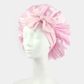 Detailed close-up of pink satin sleep cap with a large decorative bow on model head - One Size / Pink