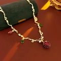 Dettaglio di una collana con fragola, perle bianche e cristalli verdi su catena dorata - Collana con Ciondolo a Fragola