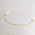 Goldene Büroklammer-Kette und weiße Perlenkette mit Knebelverschluss auf grauem Grund - Gold