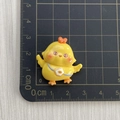 Dettaglio di un ciondolo a pulcino giallo in resina da 2,5 cm su tappetino di misura - Pulcino con le ali aperte