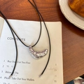 Collier minimaliste pendentif croissant avec cordon en cuir noir sur un livre - Argenté