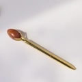 Macro detail of golden metal ballpoint pen featuring a claw-set red quartz gemstone egg - Sunstone