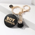 Makroansicht goldener BOY MAMA Schlüsselanhänger mit schwarzer Quaste auf Geometrie - Schwarz