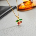 Elegant gold cherry pendant necklace with red and green crystals on a textured surface - Red Cherry Necklace 0368