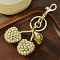 Llavero de cereza dorada con brillantes sobre una bandeja de madera rústica decorativa - Cereza con diamantes de imitación blanco dorado