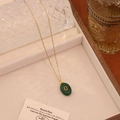 Nahaufnahme der goldenen Edelstahlhalskette mit grünem ovalem Stein auf beigem Samt - Malay-Jade