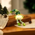 Close-up of a warm glowing Christmas gnome doll on a rustic tray with pine cones - Green Long Leg Style