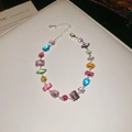 Detail of silver bracelet with multi-colored crystals and heart charm on white surface - Multicolor