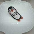 Dettaglio fermaglio per capelli a pinguino all'uncinetto su piatto di ceramica bianco - Pinguino