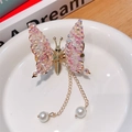 Detalle de pinza de mariposa dorada con diamantes de imitación y borlas de perlas - Rosa