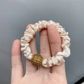 Champagne silk scrunchie with a gold rhinestone ball detail held against a gray background - Satin Beige