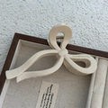 Detail view of beige glossy ribbon hair claw clip with golden text in jewelry box - Glossy White Bow Claw